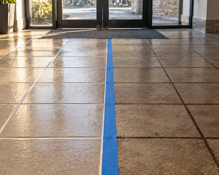 Ceramic floor tile with cleaned grout lines next to a section of dark untreated grout